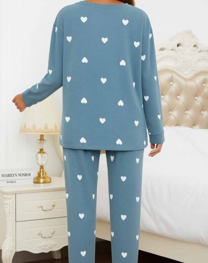 Woman in heart print pajamas sitting on a sofa with dog, lifestyle indoor photo with warm ambiance.