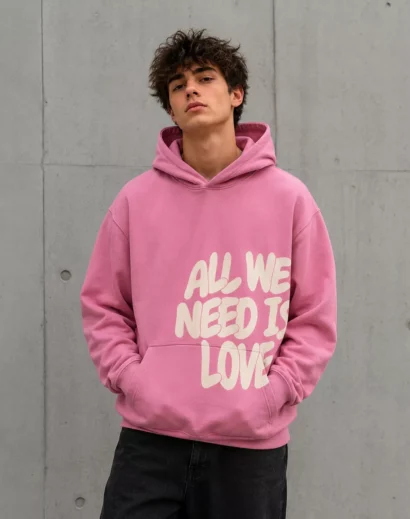 Male model wearing all we need is love hoodie pink oversized pullover front view casual streetwear style