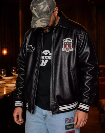 Black leather varsity jacket for men featuring a premium leather bomber design with embroidered patches. This men's leather varsity jacket showcases an oversized leather varsity jacket fit inspired by the iconic Avirex Leather Jacket and Avirex Varsity Jacket for modern streetwear fashion.
