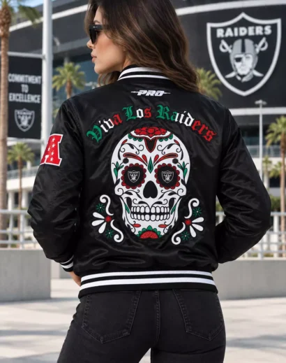 Woman wearing a women letterman jacket featuring a large embroidered sugar skull and Viva Los Raiders back design