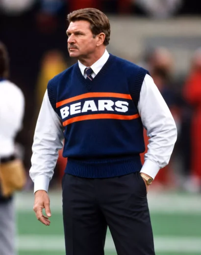 retro-football-sweater-vest-men Men's retro football sweater vest featuring white collegiate lettering and orange stripes, paired with beige trousers.